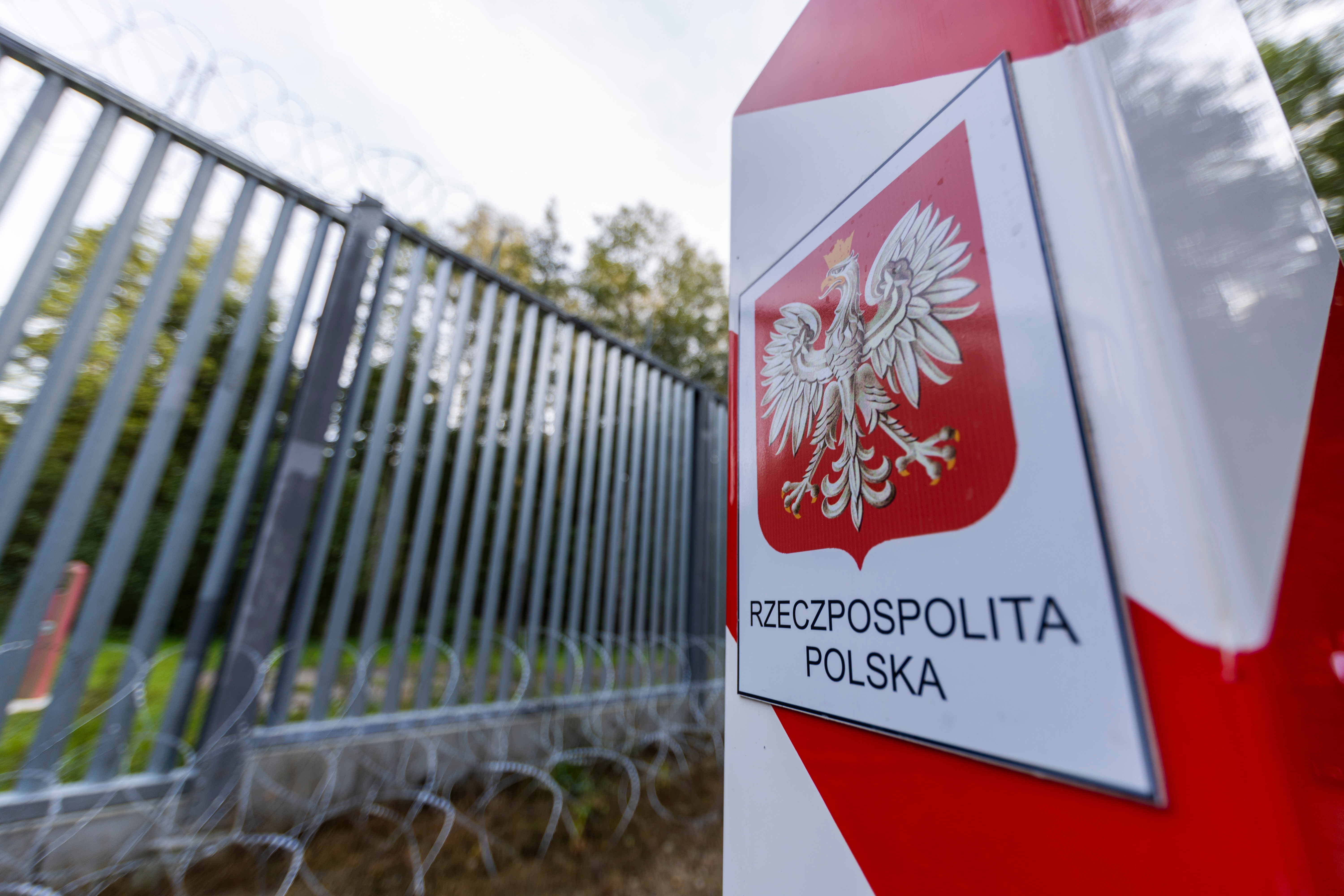 A sign for the Polish border in front of a fence